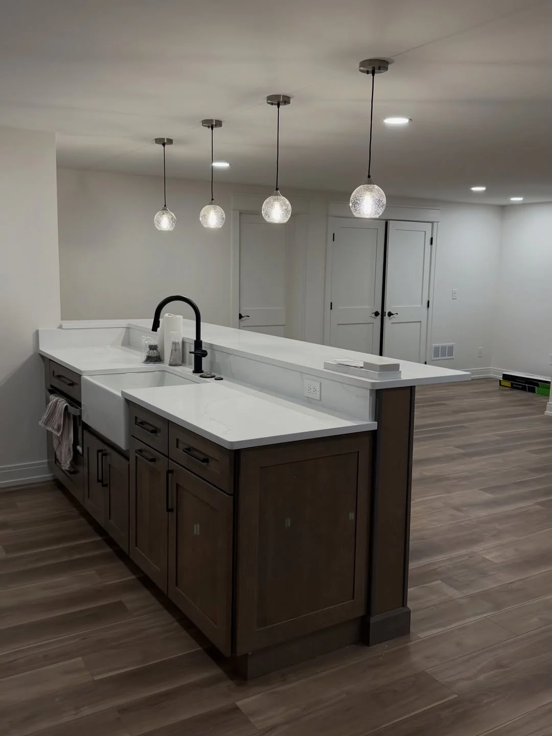 Dark wood island with white quartz countertop, dual sink, black faucet, and glass pendant lights in finished basement