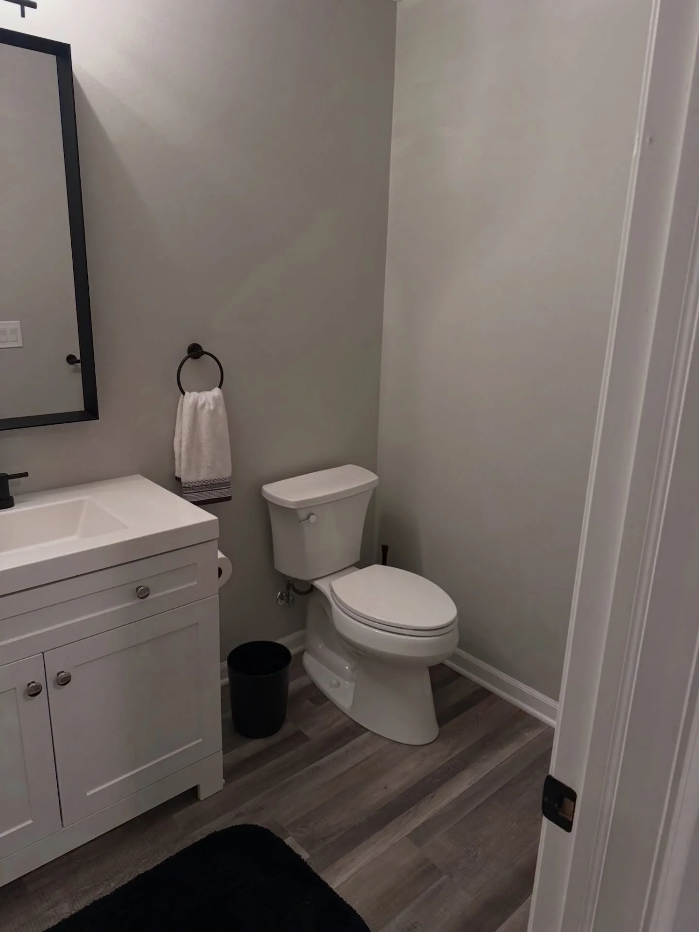 Finished basement bathroom with white vanity, toilet, vinyl plank flooring, and neutral walls