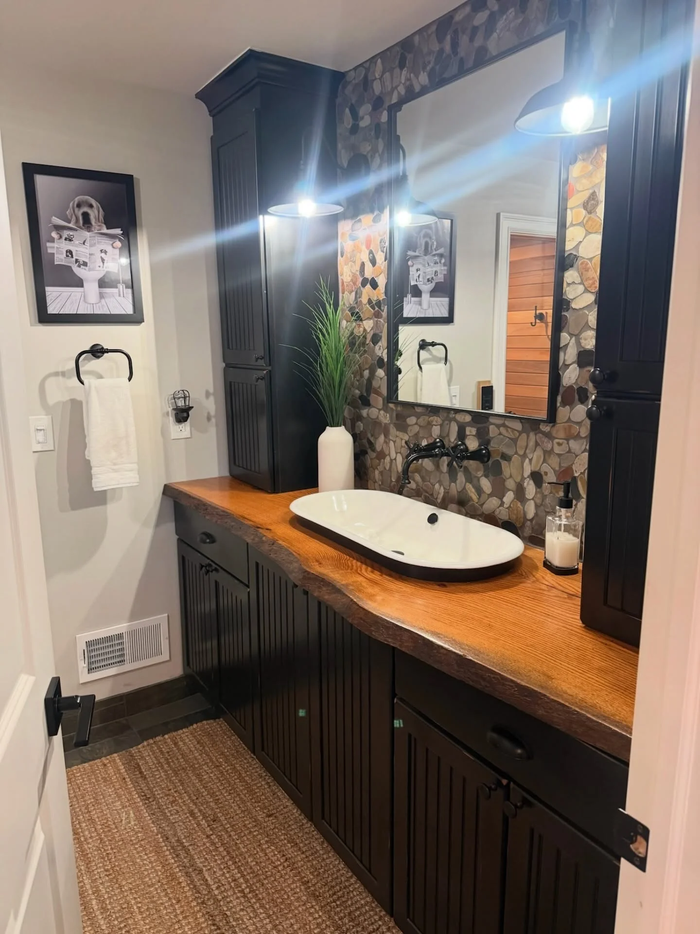 Black cabinetry vanity with live-edge wood countertop, white vessel sink, stone tile accent wall, and LED lighting