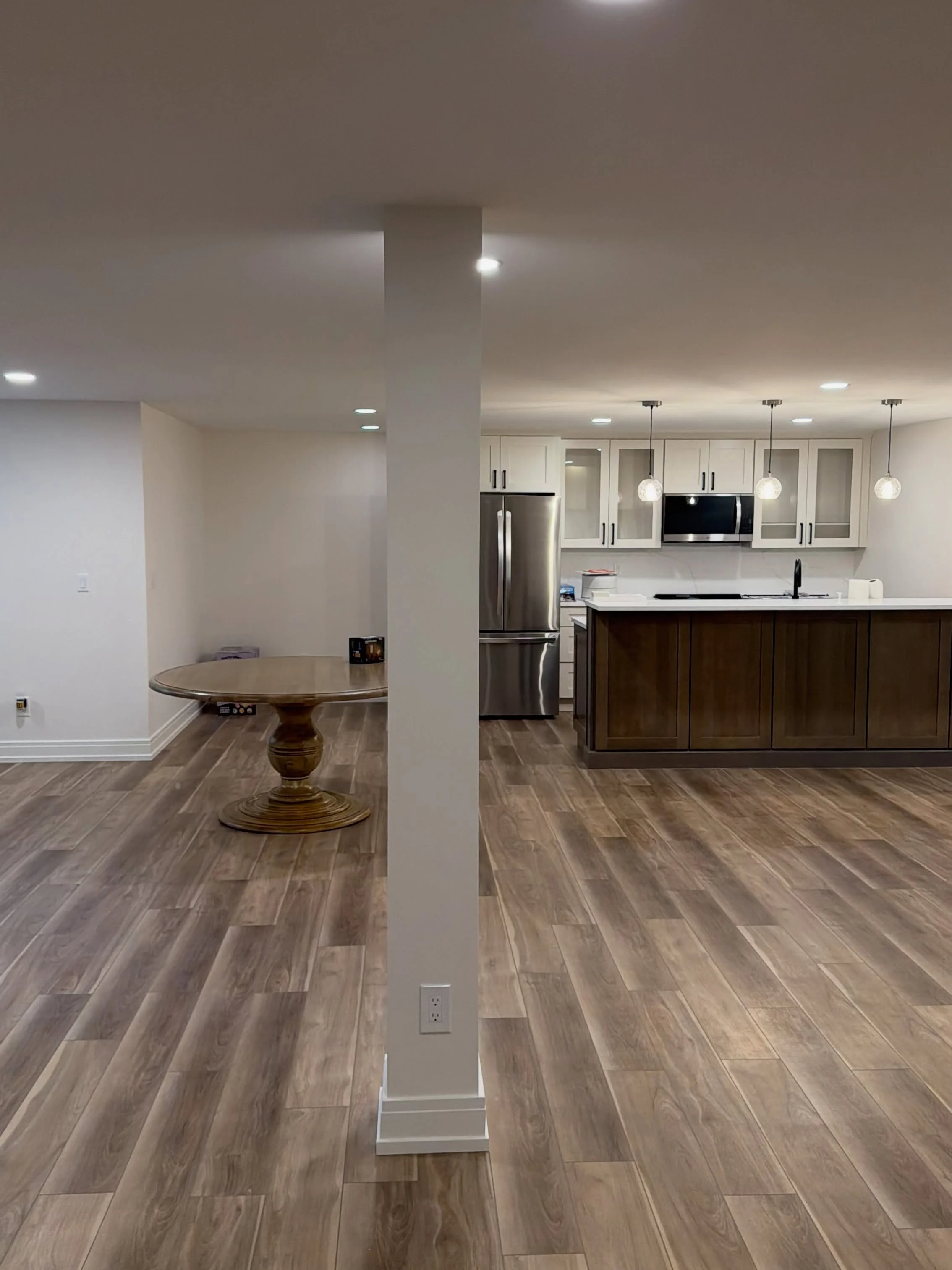 Finished basement with vinyl plank flooring, white and dark wood cabinetry, stainless steel appliances, and pendant lighting