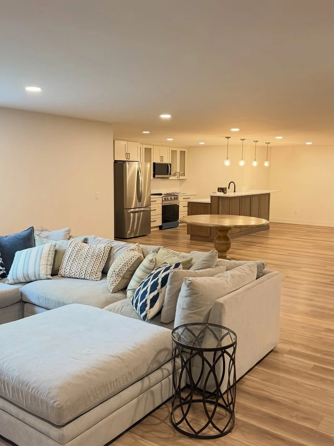 Finished basement with white cabinetry, stainless steel appliances, hardwood flooring, and pendant lighting