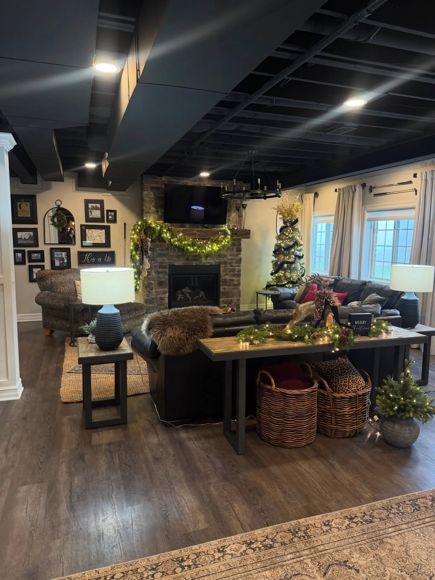Finished basement with black drop ceiling, stone fireplace, hardwood floors, and custom furnishings