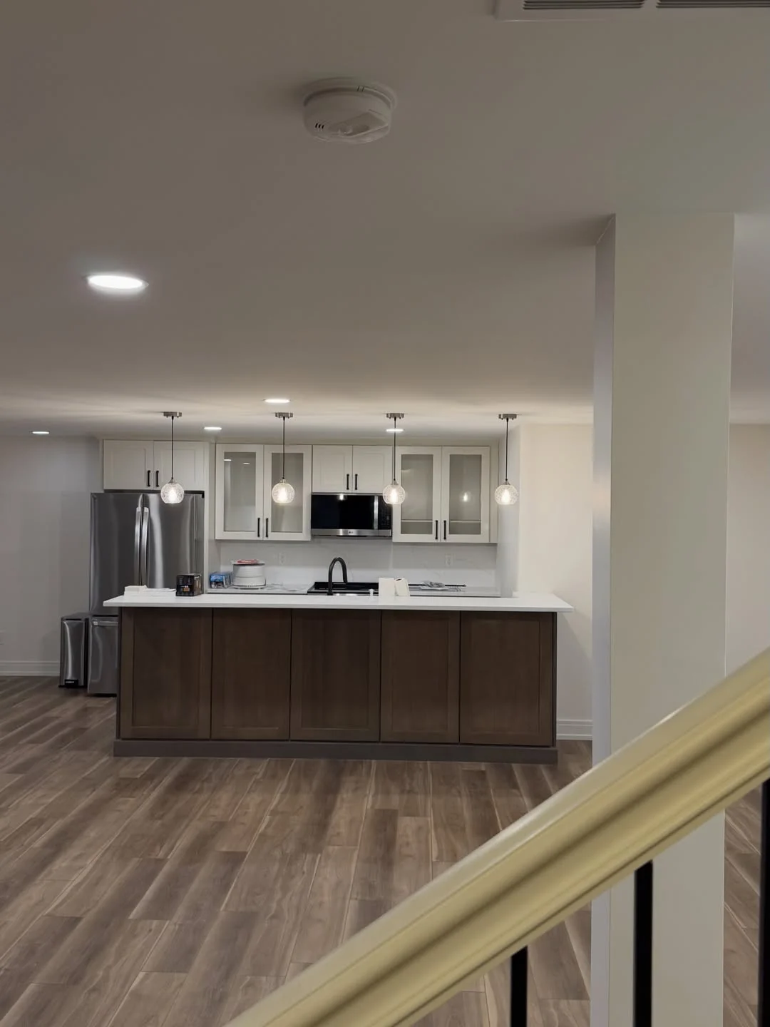 Modern basement kitchen with dark wood cabinets, white counters, pendant lights, and vinyl plank flooring