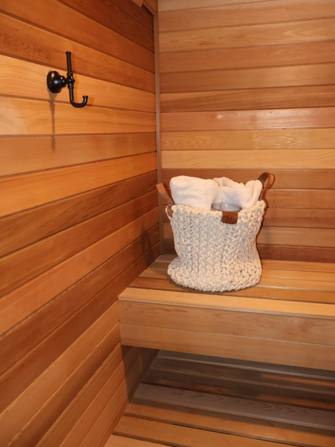 Cedar wood sauna interior with horizontal paneling, built-in bench, and black metal hook