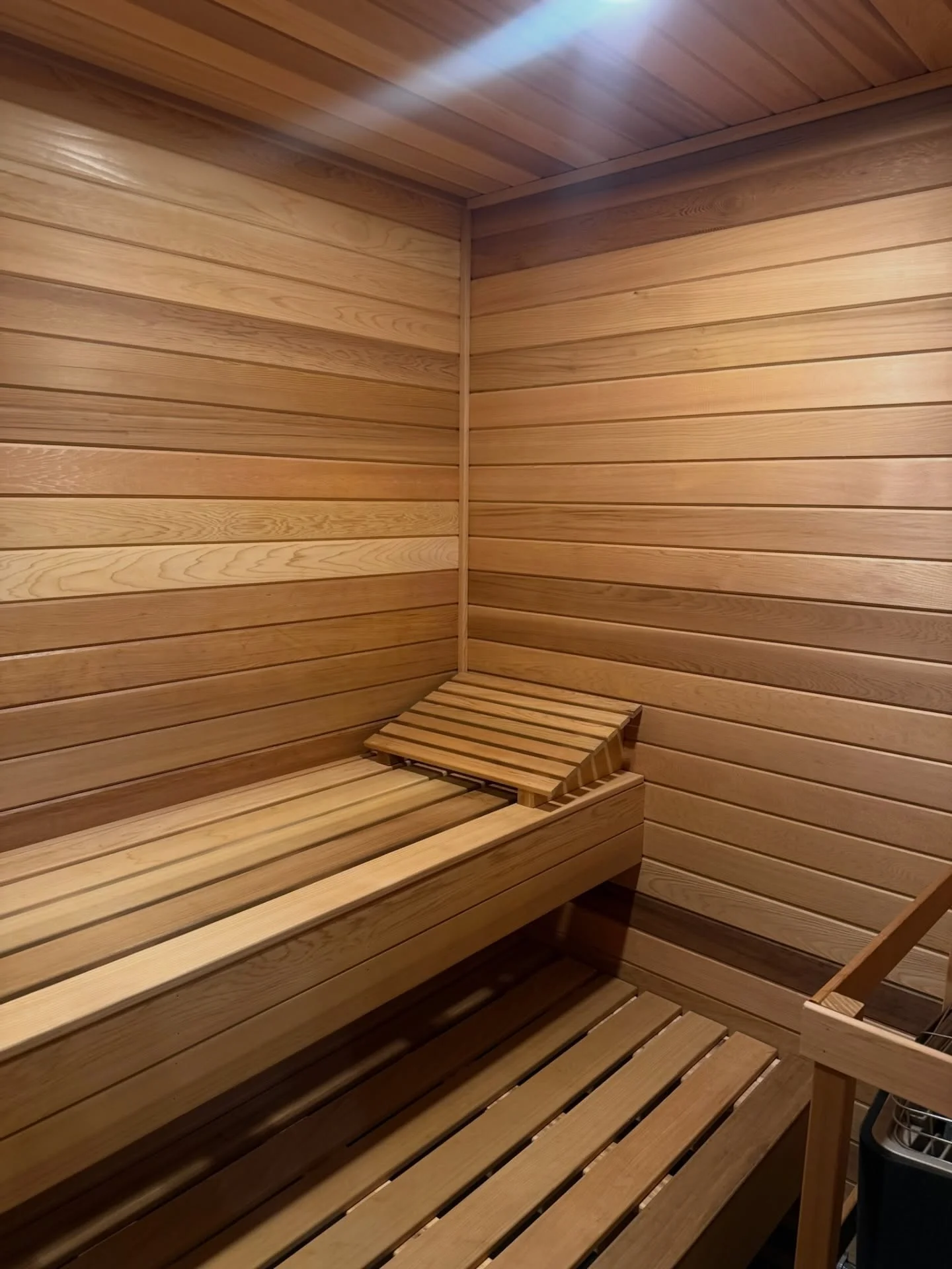 Interior sauna with horizontal wood plank walls, ceiling, and tiered wooden bench seating